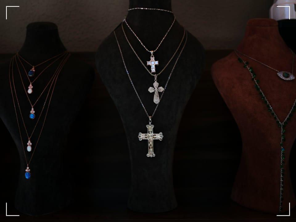 Image of three mannequins with necklaces. The center mannequin is black with 3 silver necklaces with crosses..